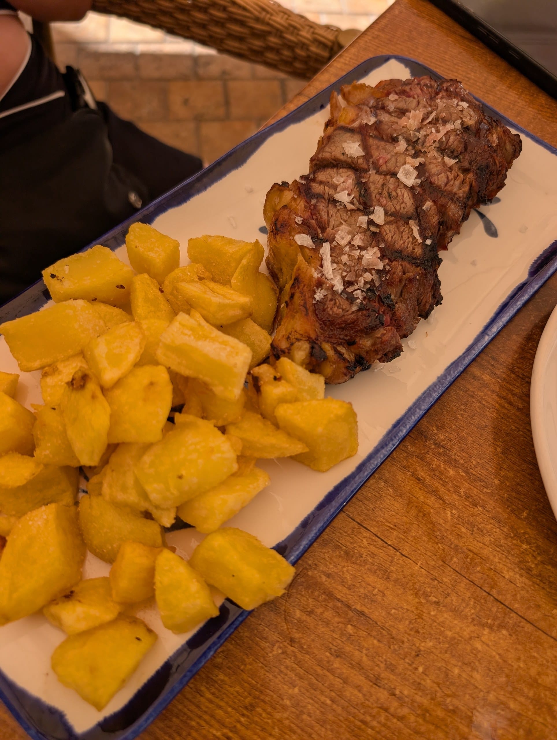 Aged beef sirloin topped with flake salt beside a plate of fried potatoes at El Pimpi in Málaga