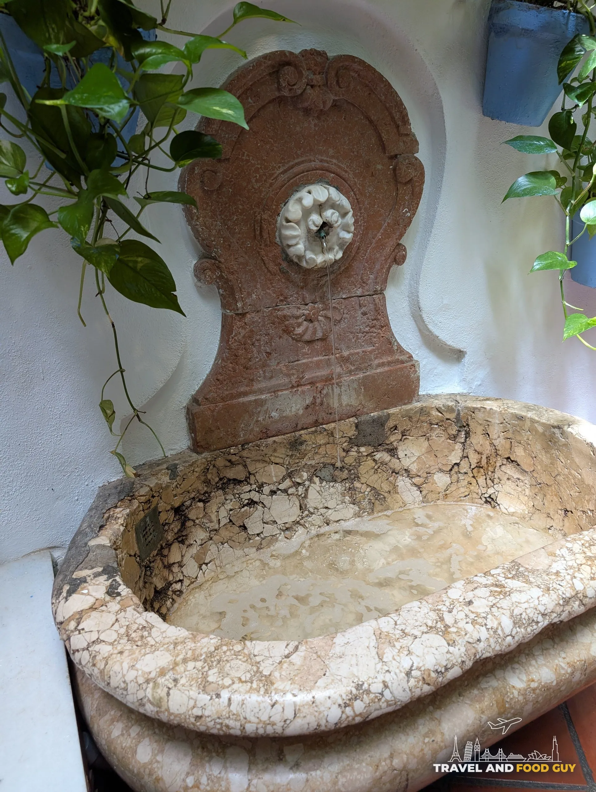 Carved marble wall fountain with running water in a corner at El Pimpi in Málaga