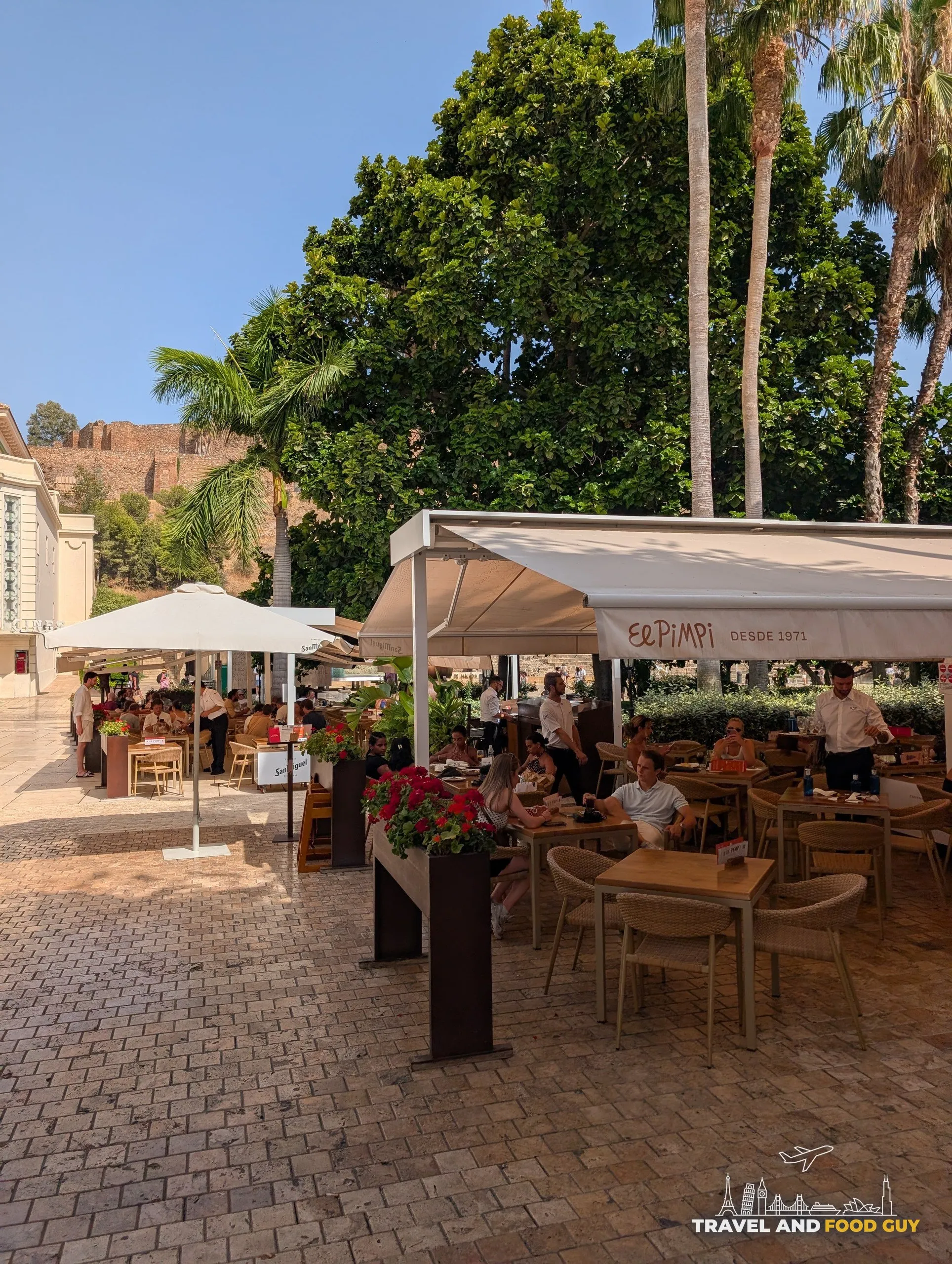 Shaded El Pimpi terrace with awnings reading Desde 1971 and the Alcazaba on the hill behind
