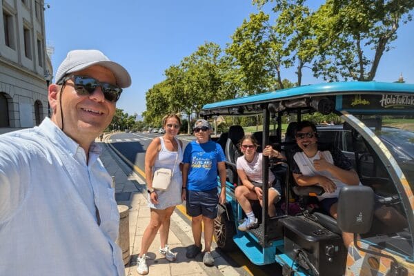 Alex, Vika, Josh, and Emily with guide Leo beside the blue HolaTukTuk electric tuk tuk in Barcelona