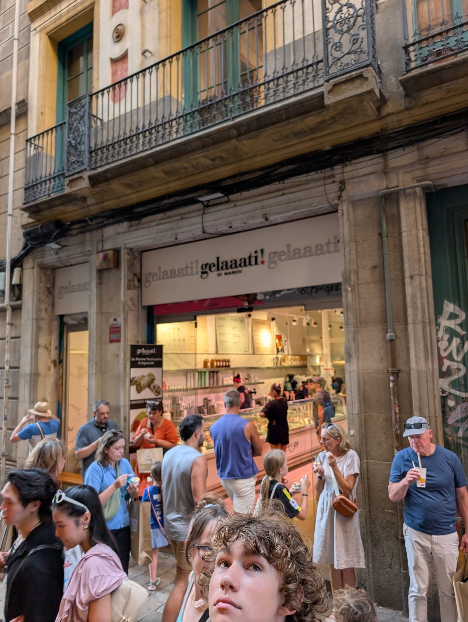 The Gelaaati DI MARCO storefront on Carrer de la Llibreteria in Barcelona with a crowd of people eating gelato on the narrow street