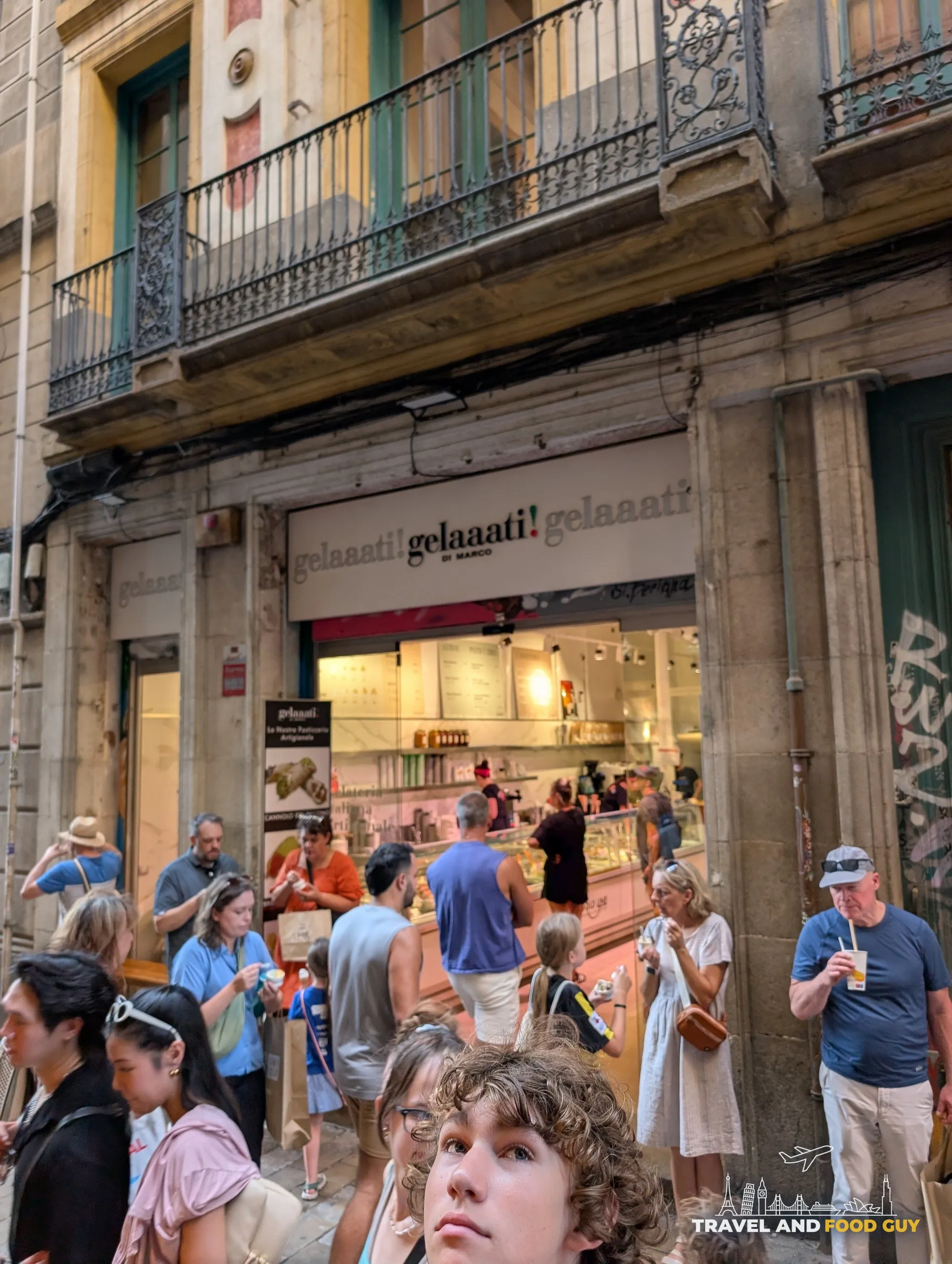 The Gelaaati DI MARCO storefront on Carrer de la Llibreteria in Barcelona with a crowd of people eating gelato on the narrow street