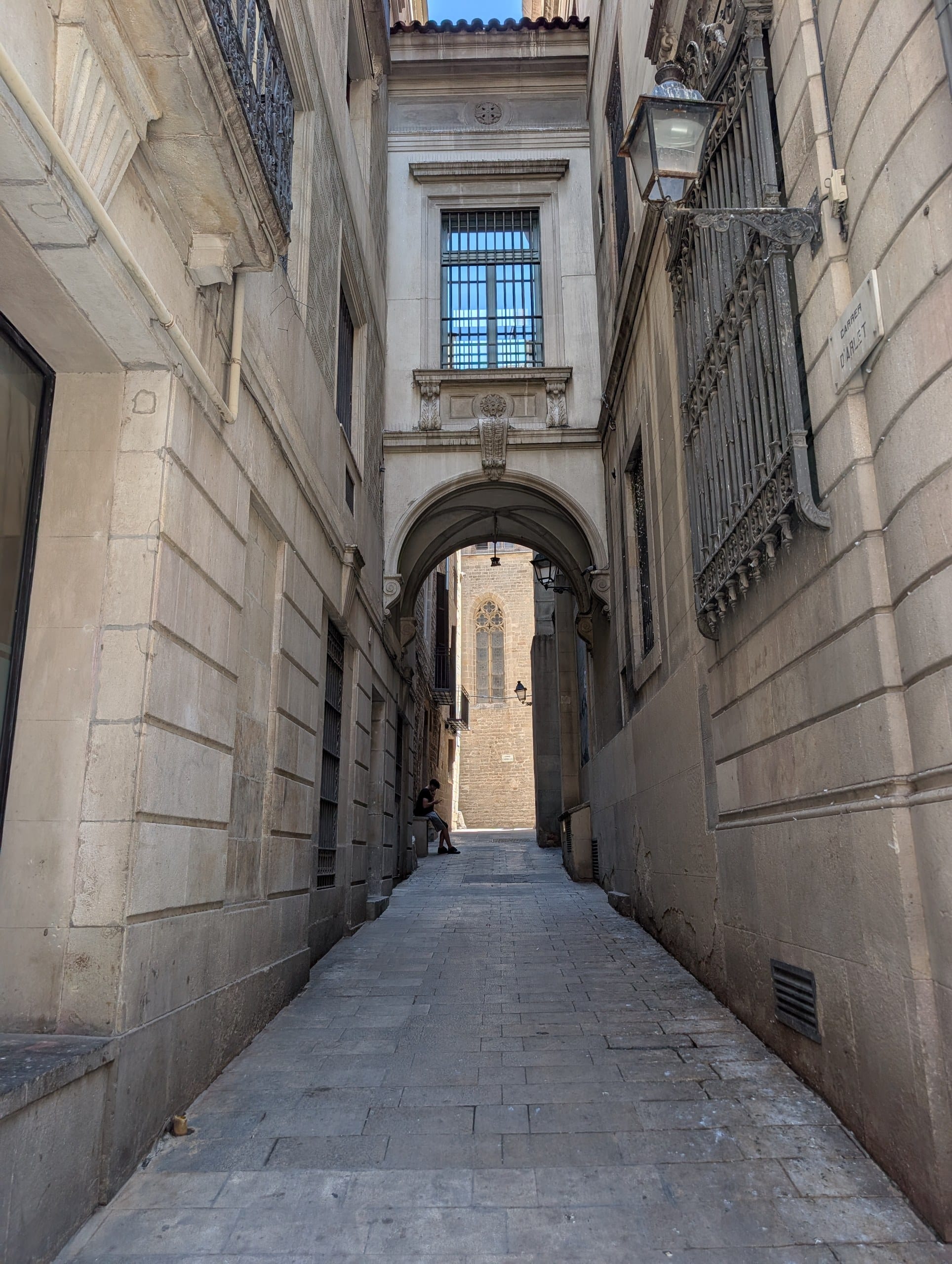 A stone arch over a shaded lane in the Gothic Quarter of Barcelona with pigeons on the ground