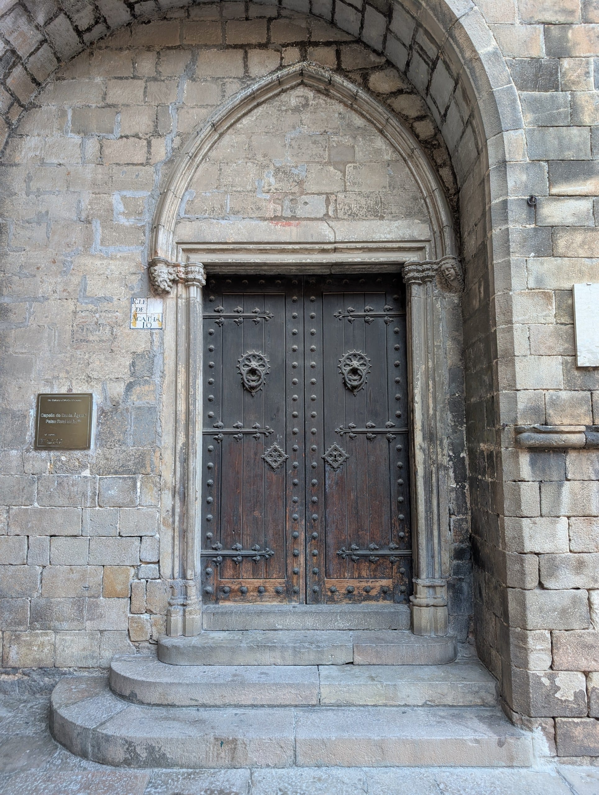 A Gothic arched doorway with a carved stone plaque beside it in the Gothic Quarter of Barcelona