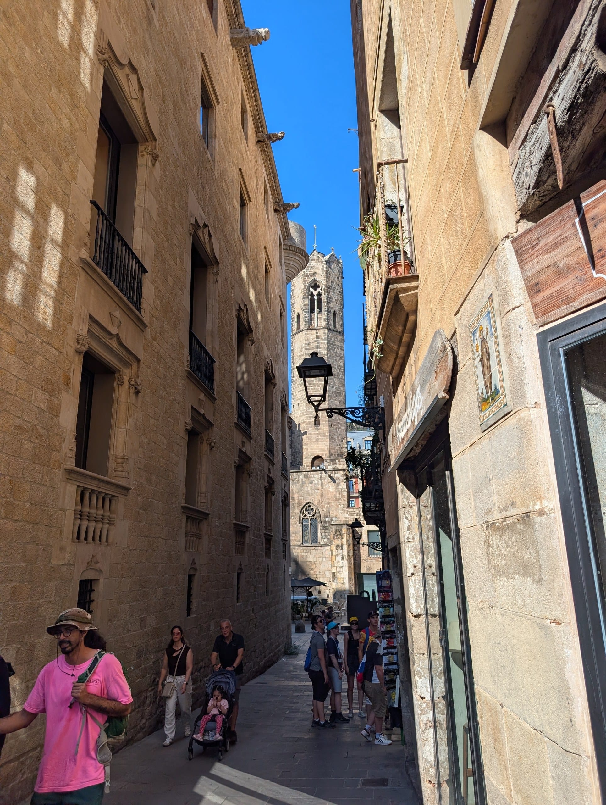 A narrow street in the Gothic Quarter of Barcelona with a stone bell tower rising at the end of it