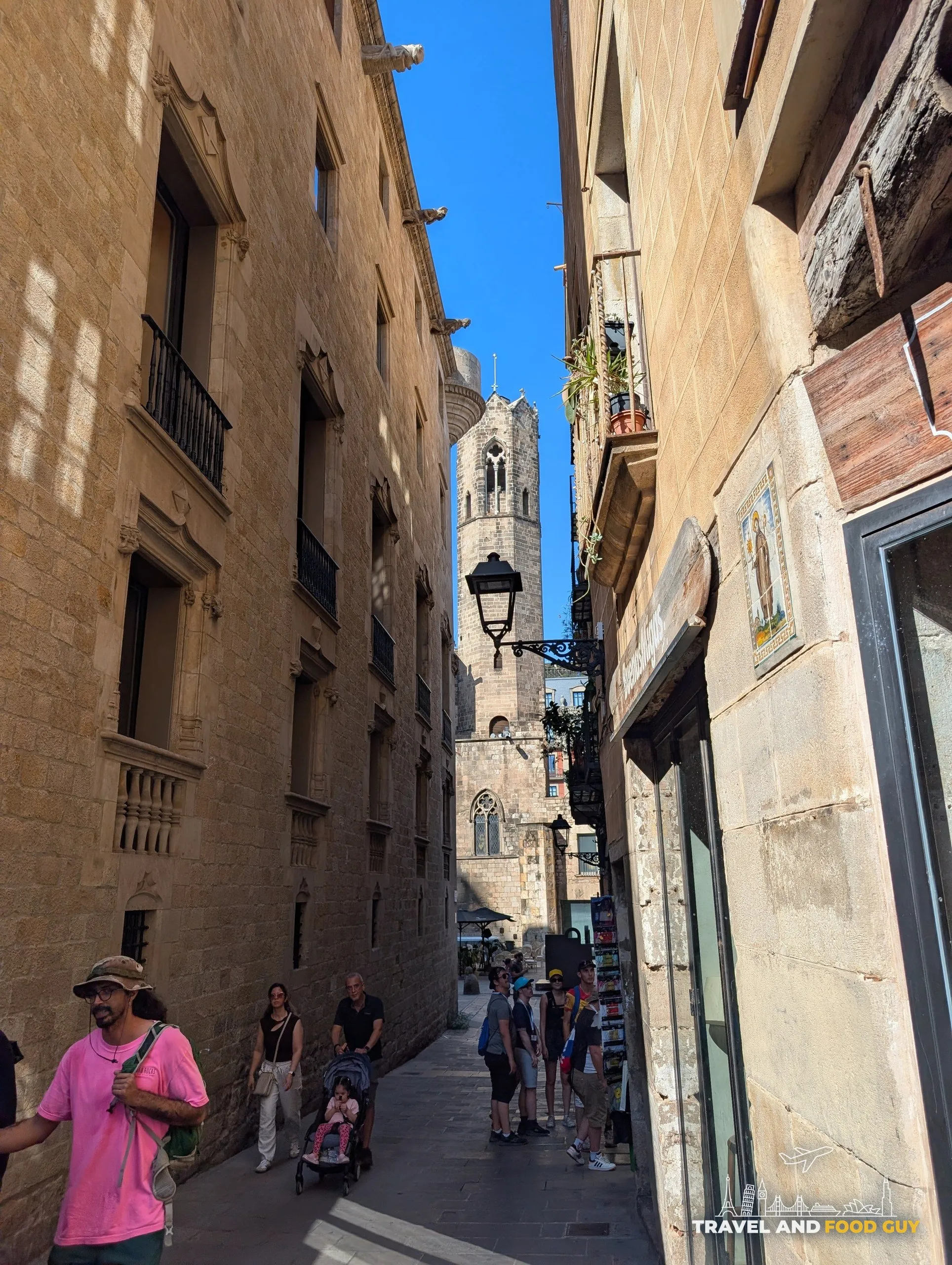 A narrow street in the Gothic Quarter of Barcelona with a stone bell tower rising at the end of it