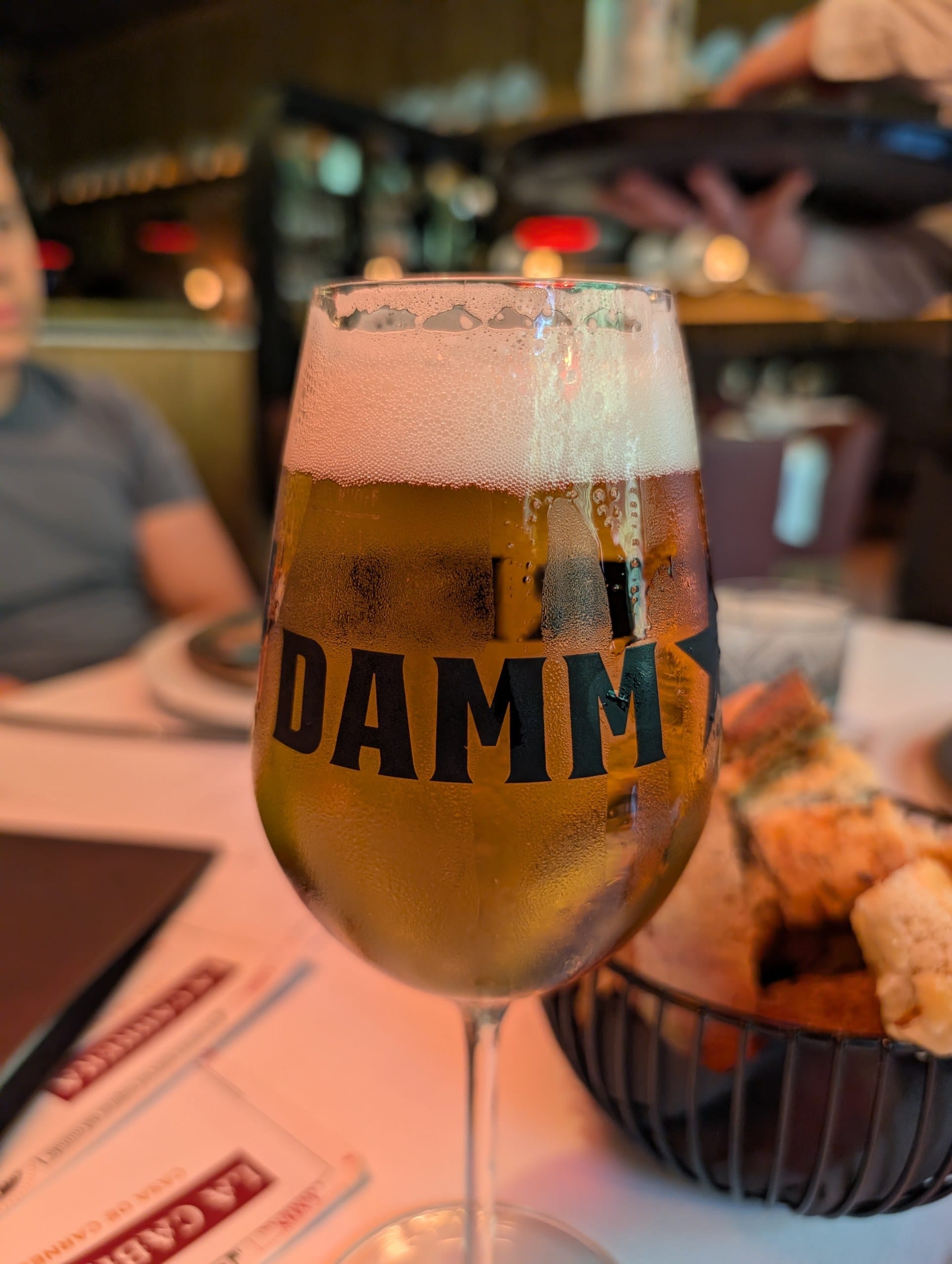 A glass of Estrella Damm beside the bread basket at La Cabrera Barcelona