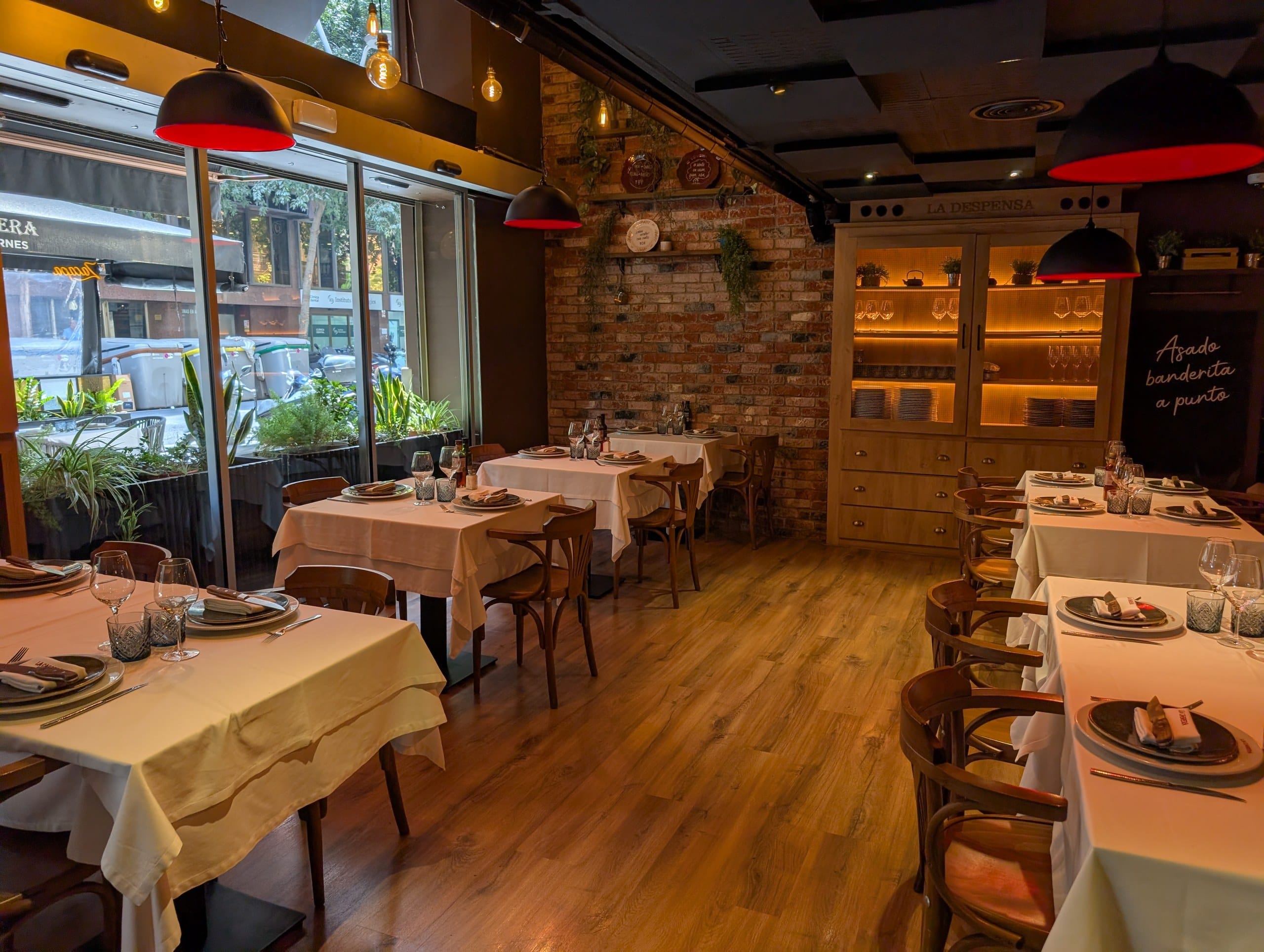 The front dining room at La Cabrera Barcelona with white linen tables and exposed brick