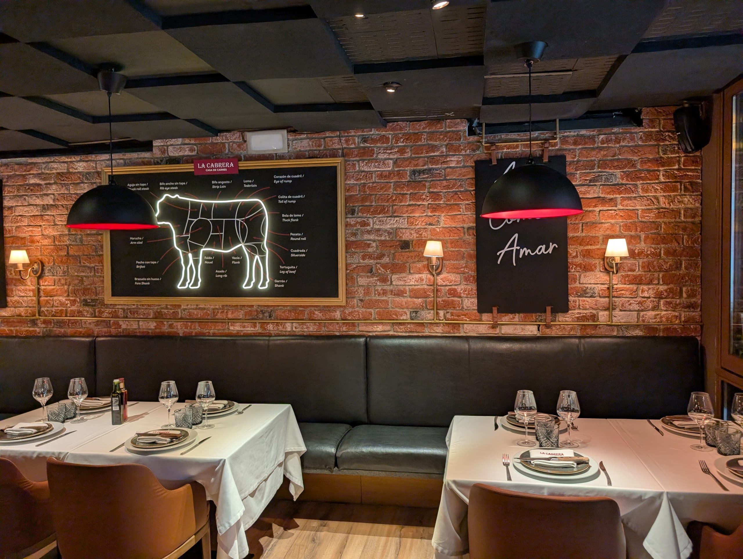 A lit diagram of Argentine beef cuts on the brick wall above the banquette at La Cabrera Barcelona