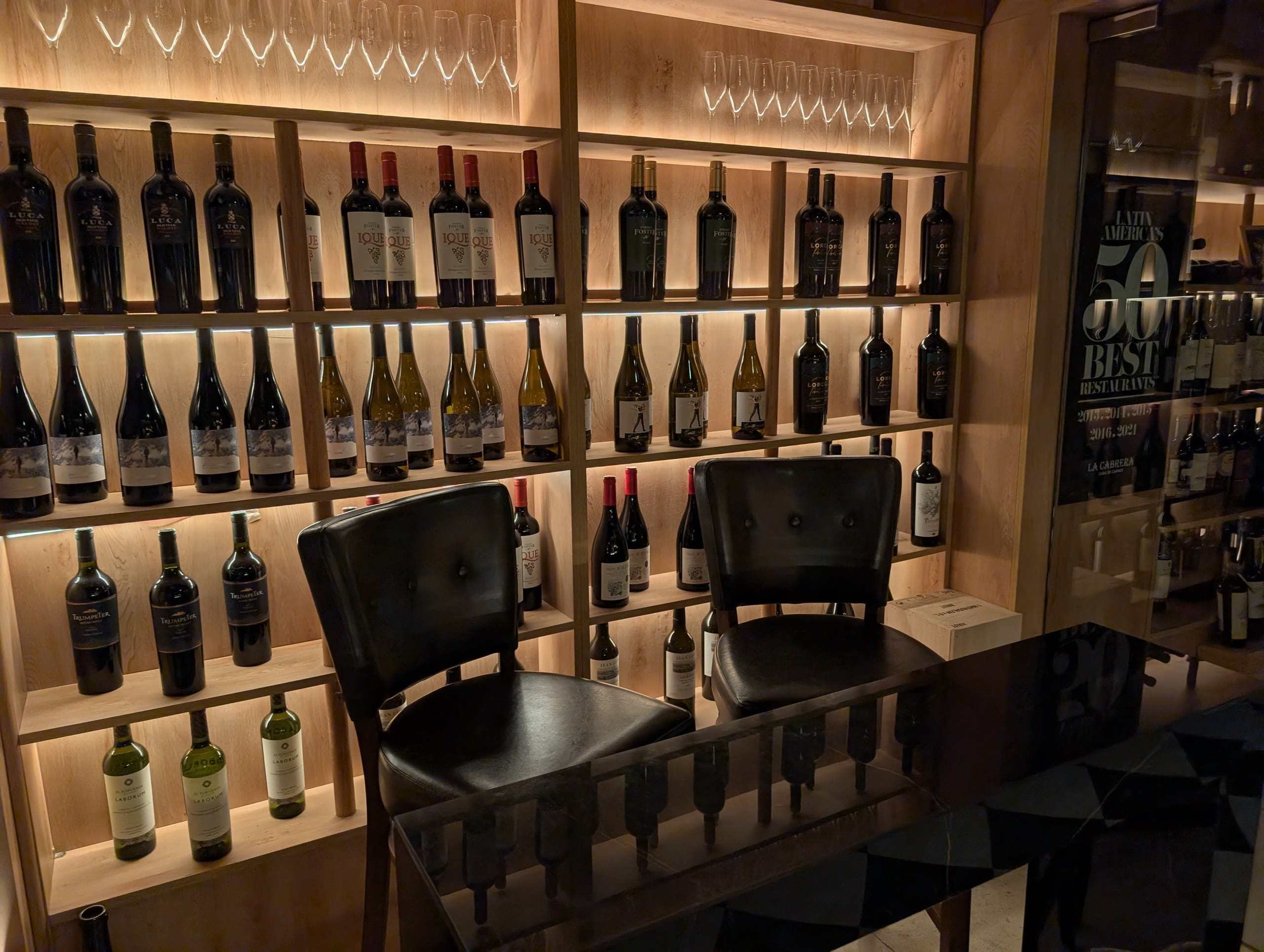 The lit wine wall at La Cabrera Barcelona beside the Latin Americas 50 Best Restaurants plaque