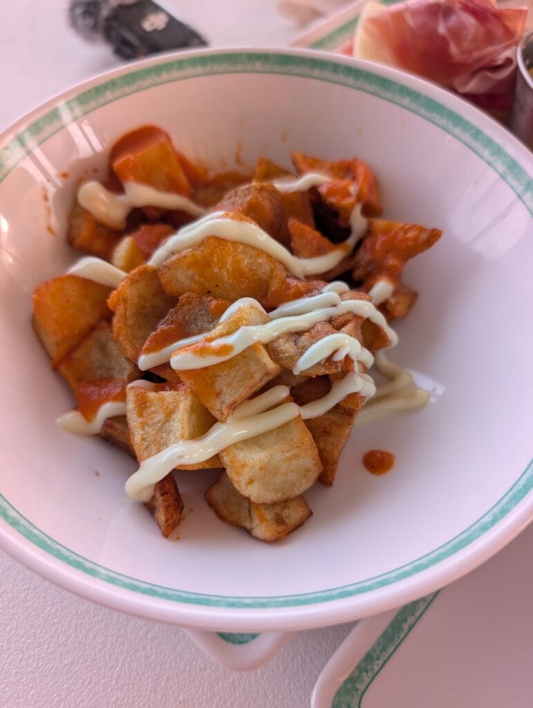 A bowl of patatas bravas from La Espanola on Legend of the Seas, brava sauce underneath and white aioli drizzled over the top.