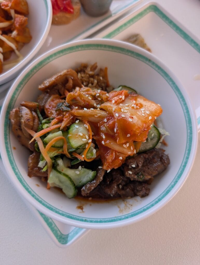 A Seoulmate bulgogi bowl on Legend of the Seas, marinated beef and rice under kimchi, cucumber, pickled carrot and white sesame.