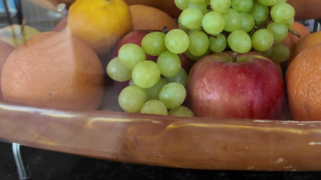 A wooden bowl of oranges, grapes, apples and lemons on the Simply Pressed counter in the AquaDome Market.