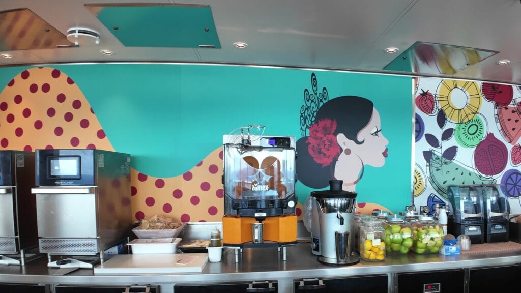 The orange press, juicer and blenders at the Simply Pressed counter in the AquaDome Market, in front of a fruit mural.