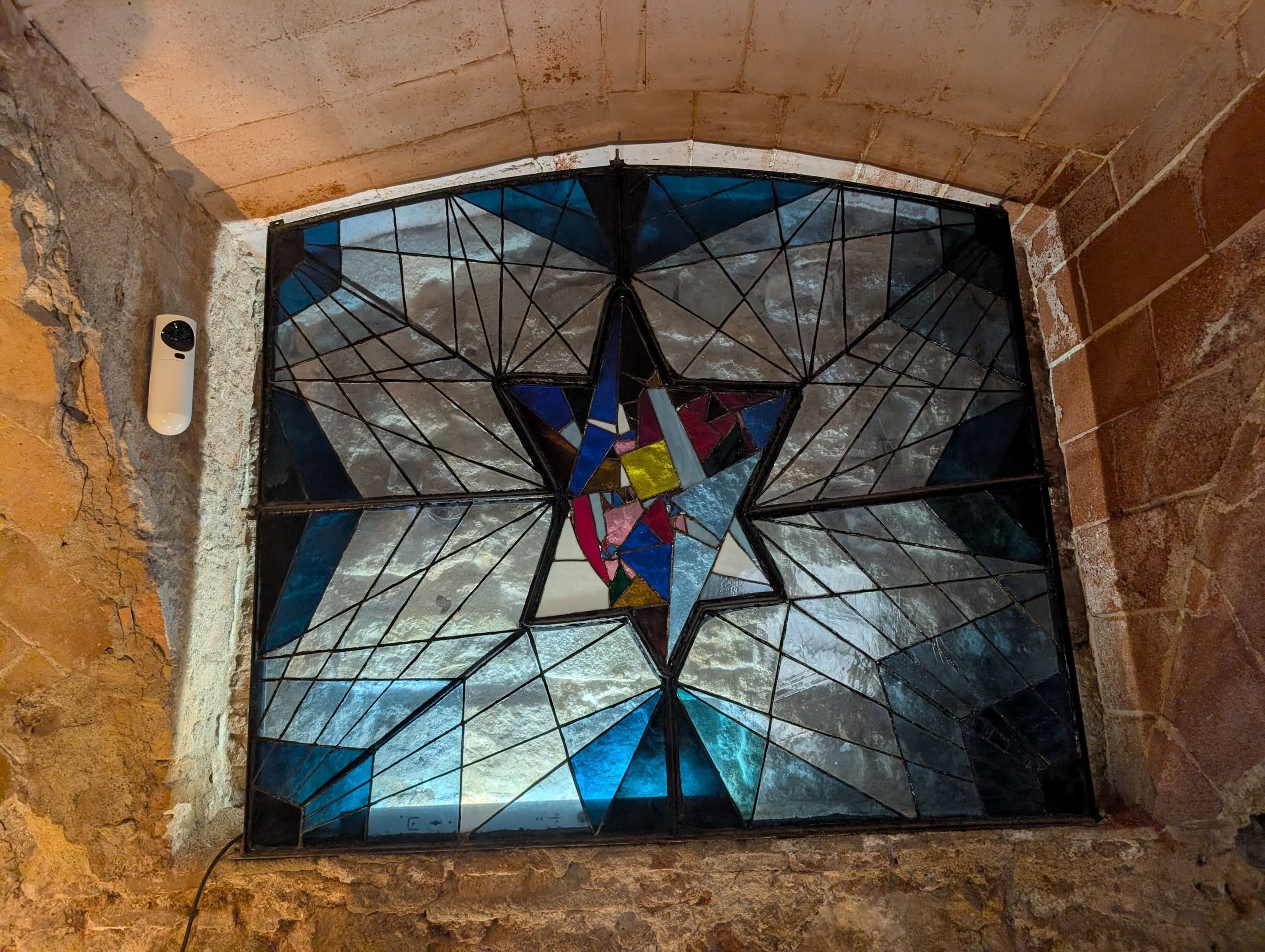A stained glass Star of David set into a rough stone vault and lit from behind at the Sinagoga Major in Barcelona