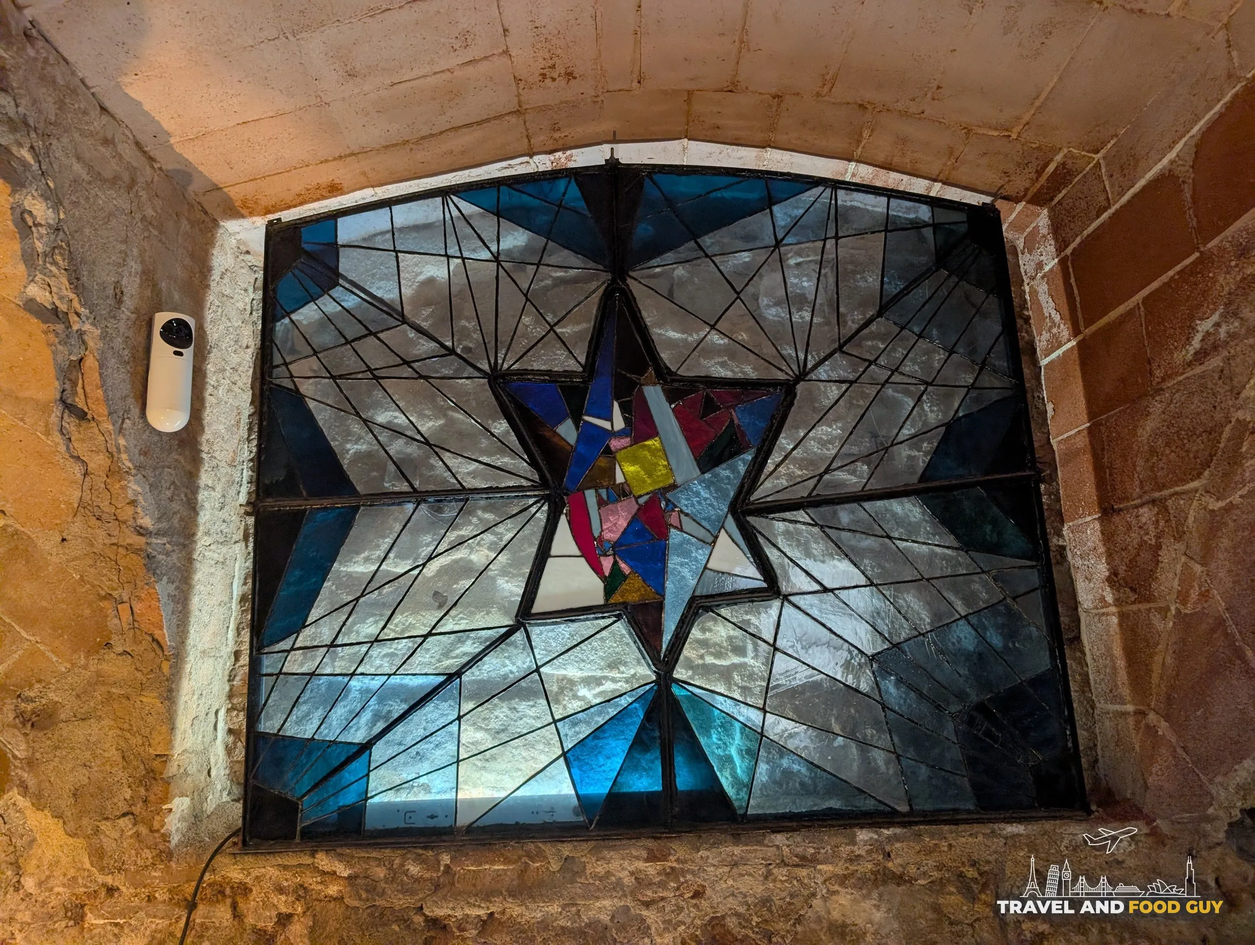 A stained glass Star of David set into a rough stone vault and lit from behind at the Sinagoga Major in Barcelona