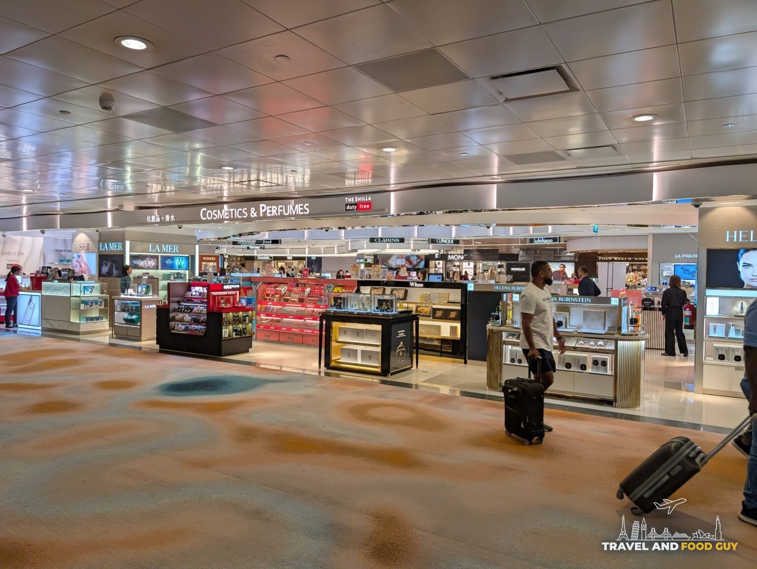 The Cosmetics and Perfumes duty free retail area at Changi Airport Terminal 2 with a traveler pulling a rolling bag through the polished terracotta terrazzo floor