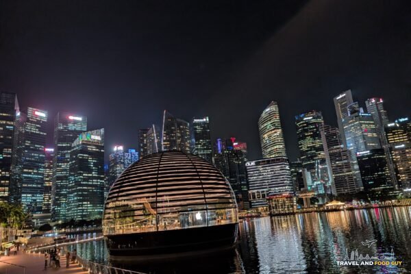 The Apple Marina Bay Sands floating dome store lit up at night with the Singapore CBD skyline reflected in Marina Bay