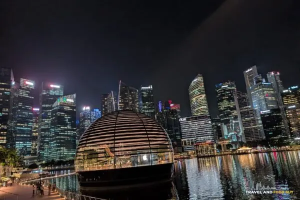 The Apple Marina Bay Sands floating dome store lit up at night with the Singapore CBD skyline reflected in Marina Bay