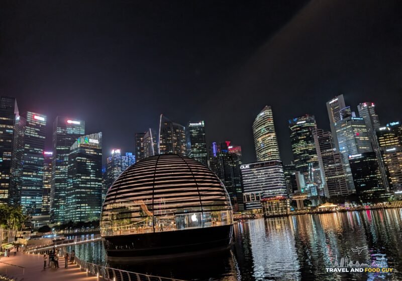The Apple Marina Bay Sands floating dome store lit up at night with the Singapore CBD skyline reflected in Marina Bay
