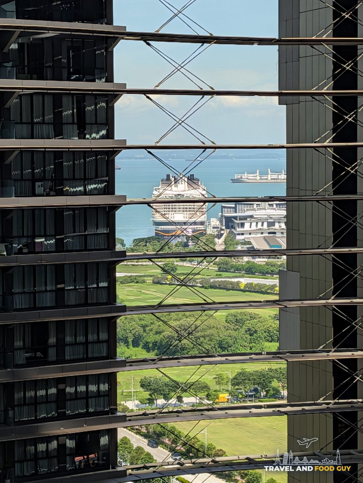 A cruise ship berthed at the Singapore Cruise Centre HarbourFront terminal, framed between the curving Reflections at Keppel Bay towers with the Strait of Singapore beyond
