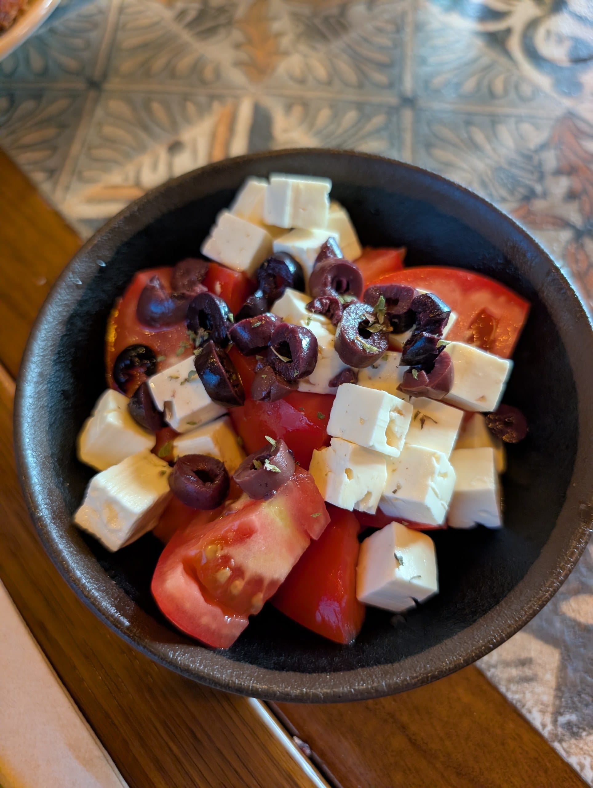 Tomato wedges with cubes of fresh white cheese, black olives and herbs in a black dish at Tapas San Miguel in Barcelona