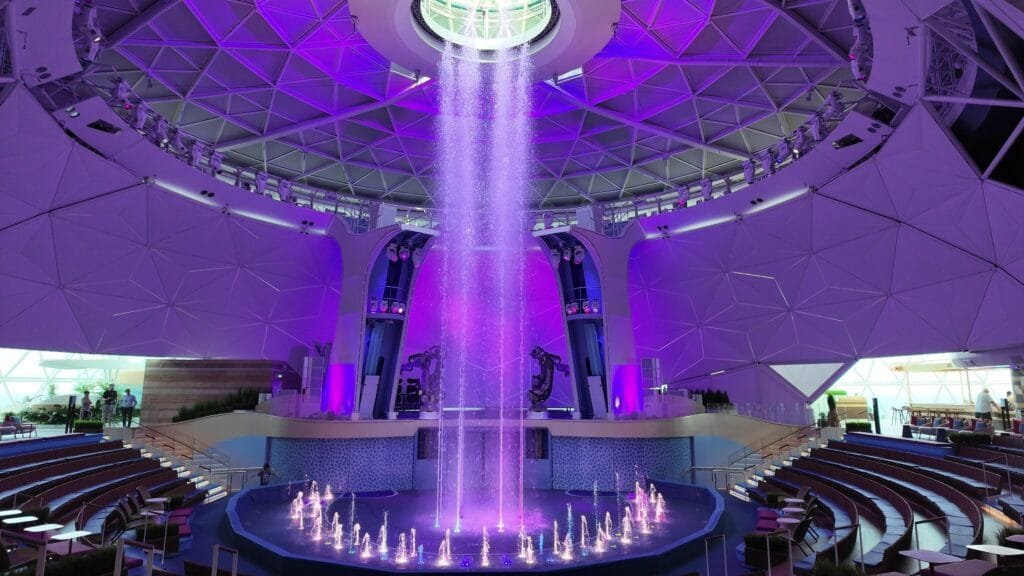 The AquaDome waterfall on Legend of the Seas, lit purple under the glass dome