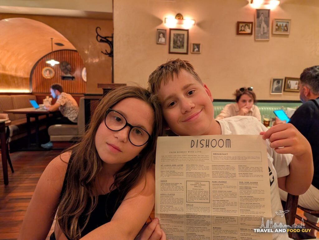 Josh and Emily at the table at Dishoom Covent Garden, Josh holding the menu.