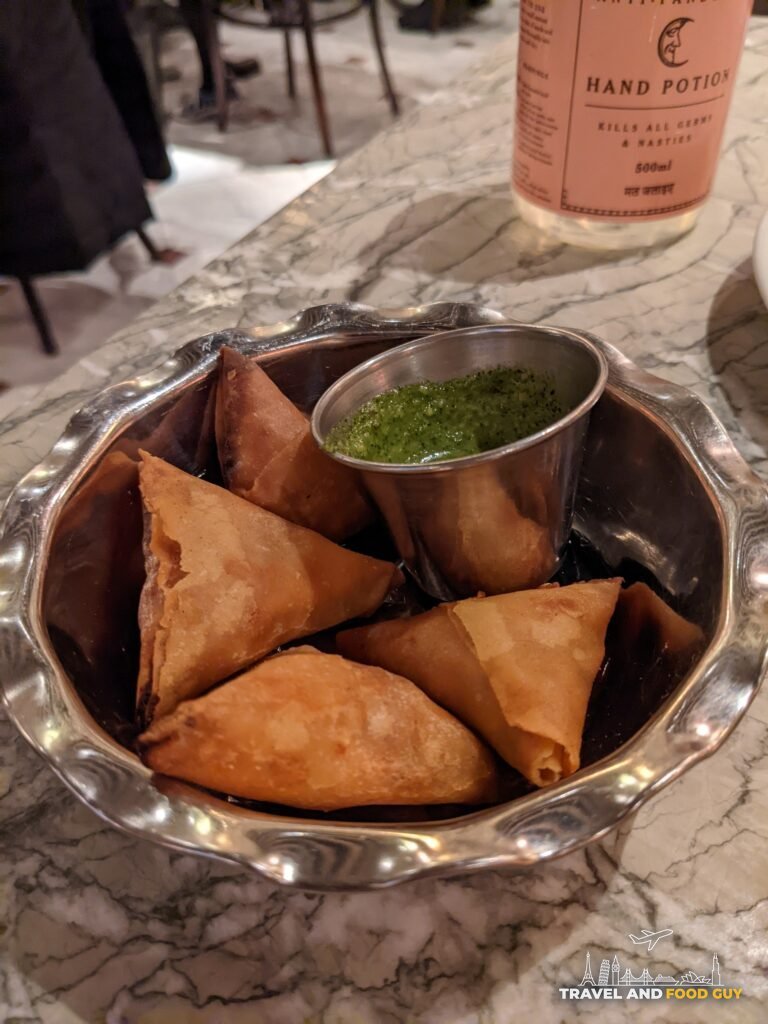 Vegetable samosas with green chutney in a silver bowl on a marble table at Dishoom Covent Garden.