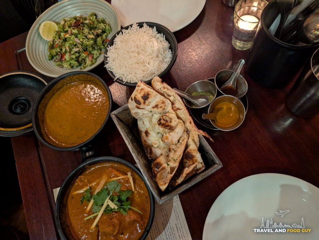 Overhead view of a Dishoom Shoreditch table for two with two curries, basmati rice, garlic naan, a chopped broccoli salad and three chutneys.