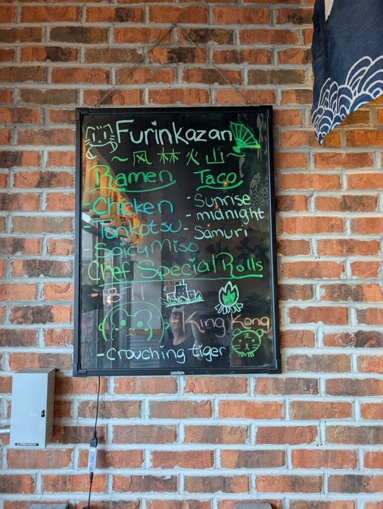 A chalkboard listing ramen, tacos and the chef special rolls including Crouching Tiger.
