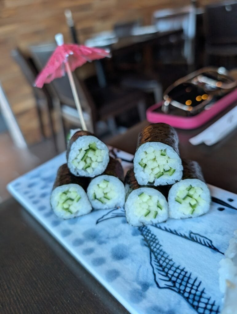 Six pieces of cucumber roll stacked on a blue and white plate with a paper umbrella.