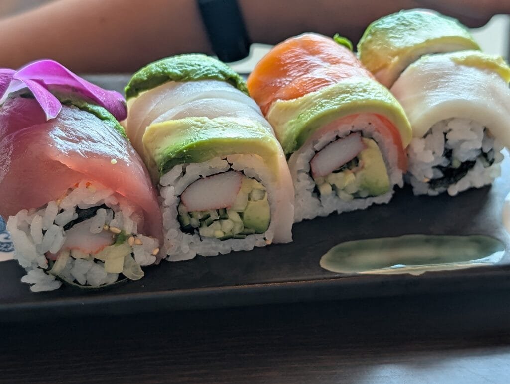 Close view of rainbow maki topped with tuna, salmon, yellowtail, white fish and avocado.