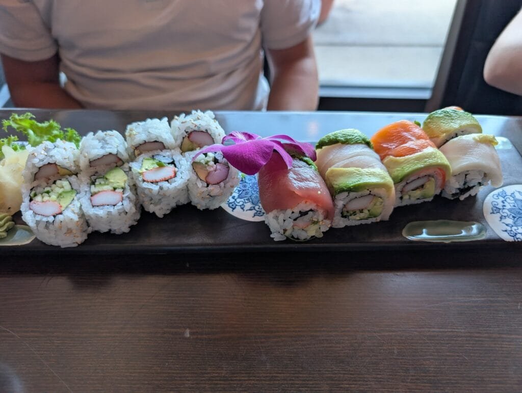 A long plate with California rolls at one end and a rainbow roll at the other, an orchid between them.