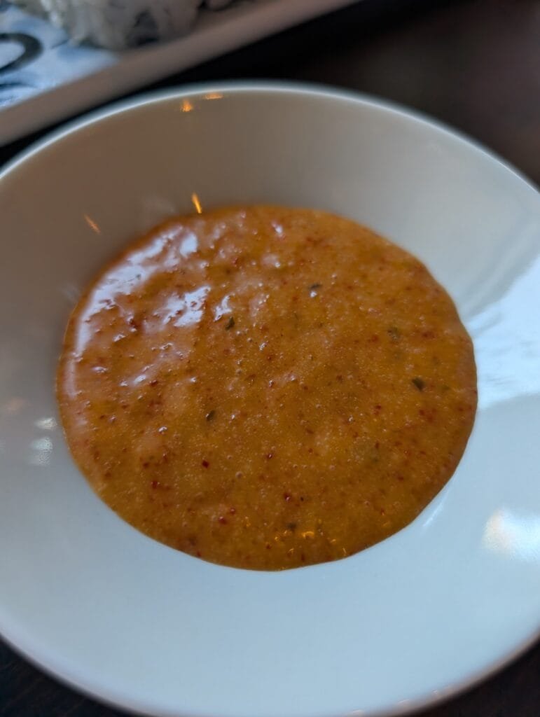 A small white dish of house spicy mayo, orange and flecked with chili.