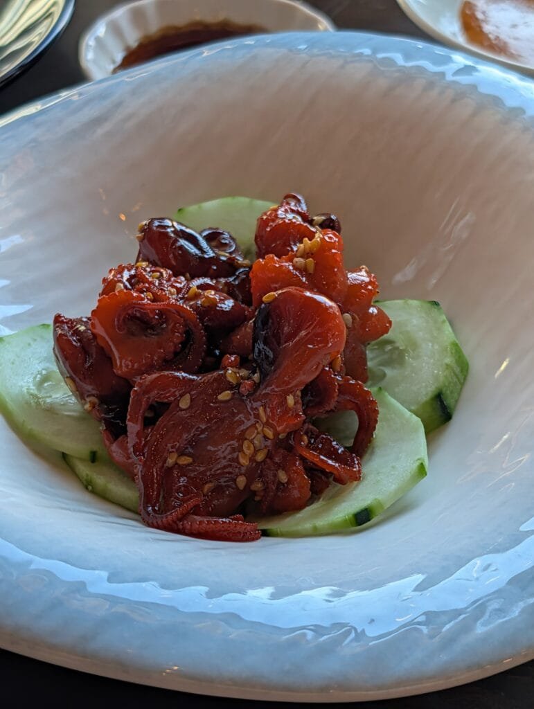 Baby octopus in a glossy red sauce with sesame seeds, served over cucumber slices.