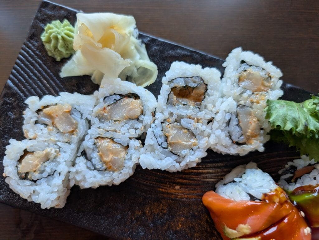 Six pieces of spicy scallop roll on a dark slate plate with pickled ginger and wasabi.