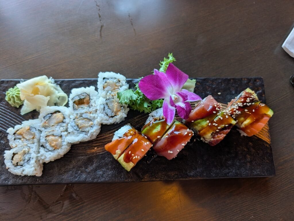The spicy scallop roll and a roll topped with salmon, tuna and eel sauce sharing one long dark plate.