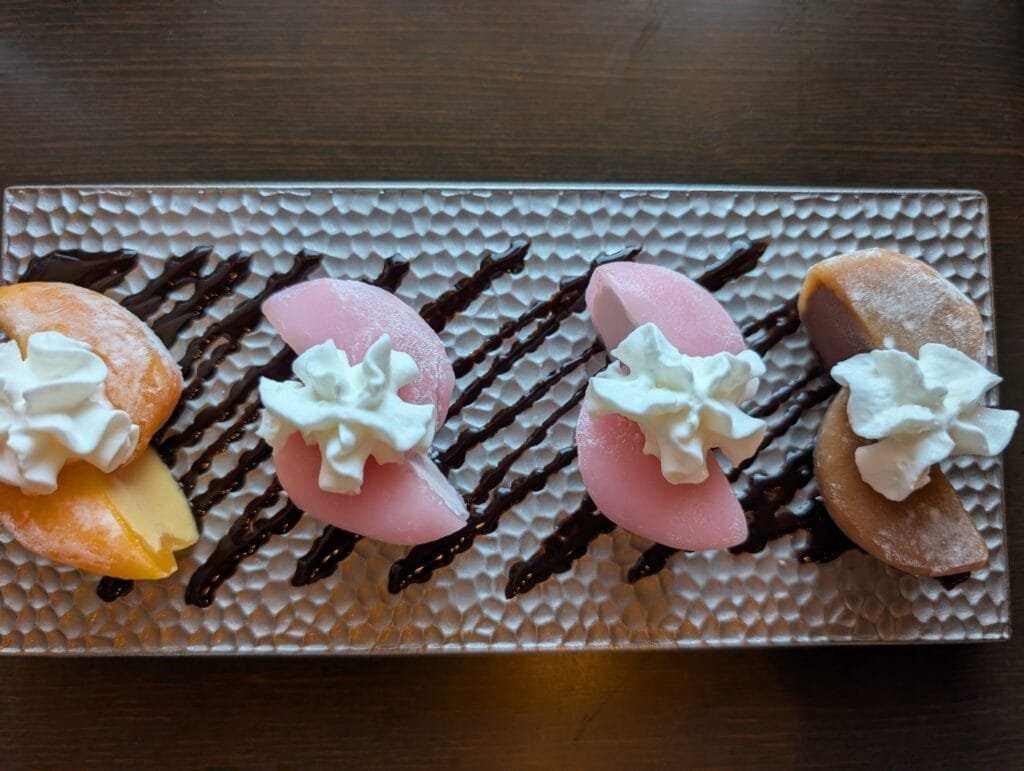 Halves of mochi ice cream on a hammered metal tray with whipped cream and a chocolate drizzle.