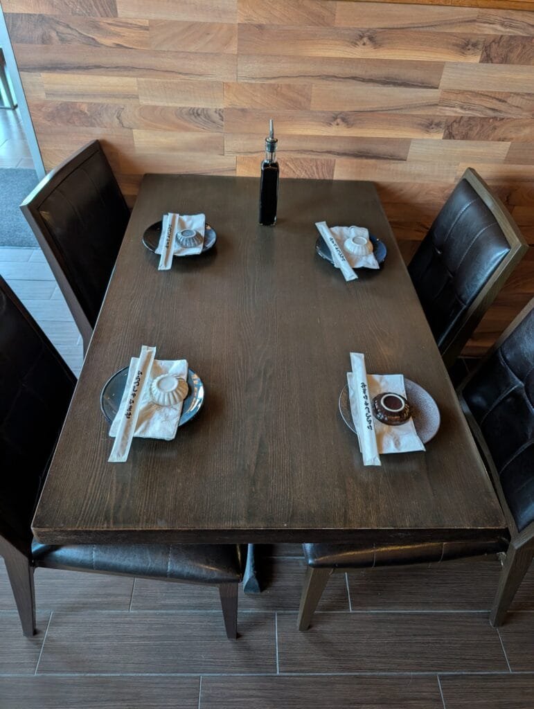 A four top set with chopsticks, folded napkins and a soy bottle against the wood plank wall.