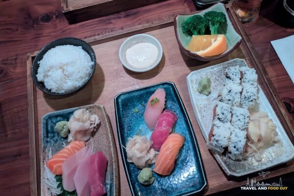 A three item bento dinner at Noma Sushi in Santa Monica with sashimi, three pieces of nigiri and a spicy tuna roll, with a bowl of rice.