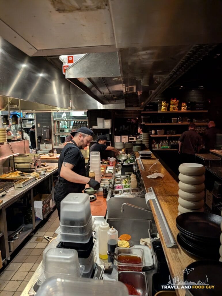 Cooks working the line in Sushi-San's open kitchen, with lucky cat figures on the shelf.