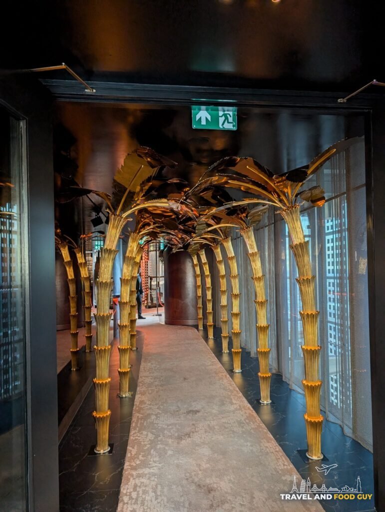 The gold palm arch corridor at SUSHISAMBA London, lit in the dark, leading from the elevator.