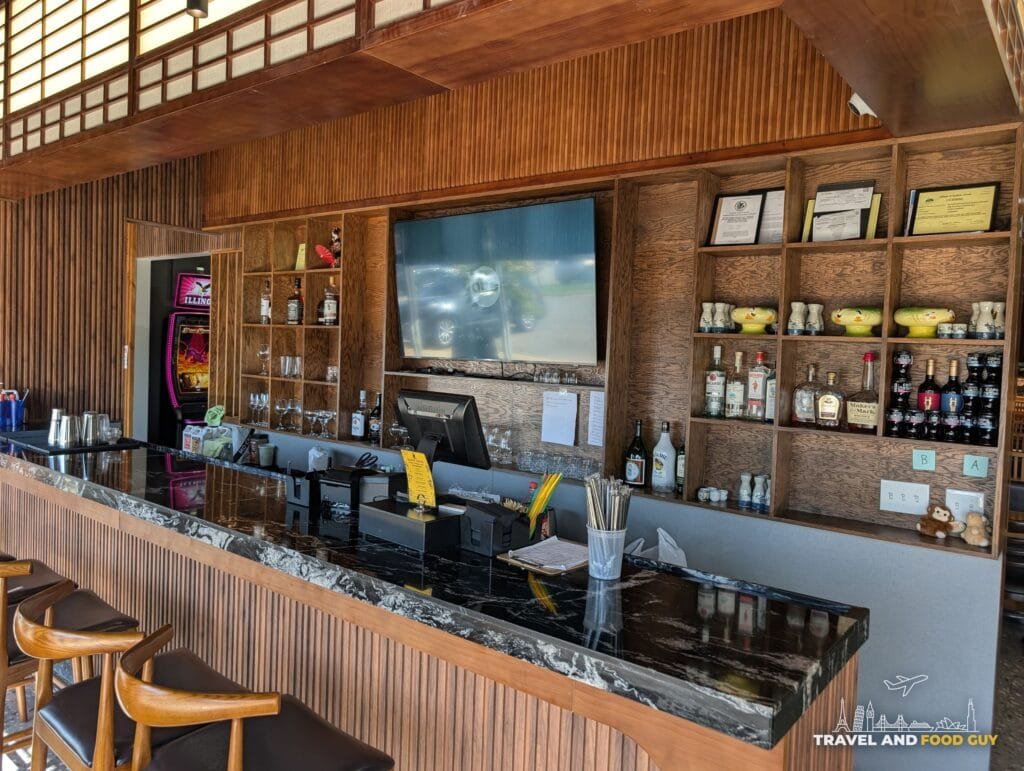 The bar at Blackfish with a dark stone counter, wooden stools, shelves of bottles and a TV.