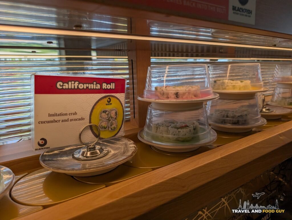 A California roll under a dome on the belt with a card that says imitation crab, cucumber and avocado.