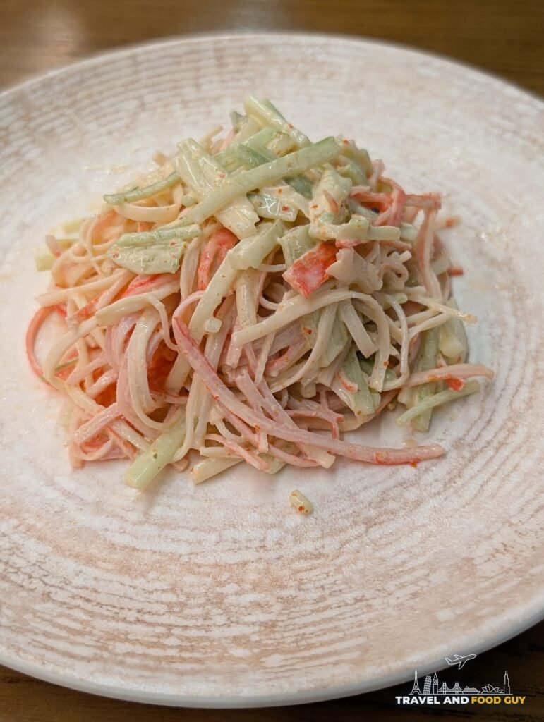 A spicy kani salad of shredded imitation crab and cucumber on a white plate.