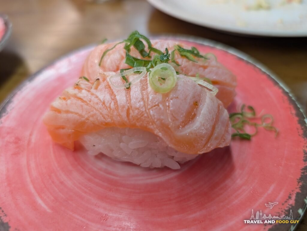 Two pieces of seared salmon nigiri topped with green onion on a pink plate.