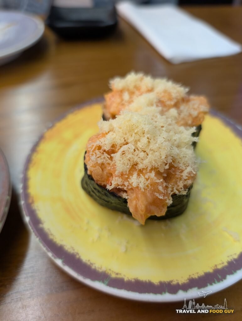 A spicy gunkan topped with crunchy tempura flakes on a yellow plate.