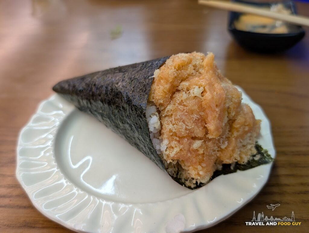A spicy salmon hand roll in seaweed on a white plate, with spicy salmon all the way down.