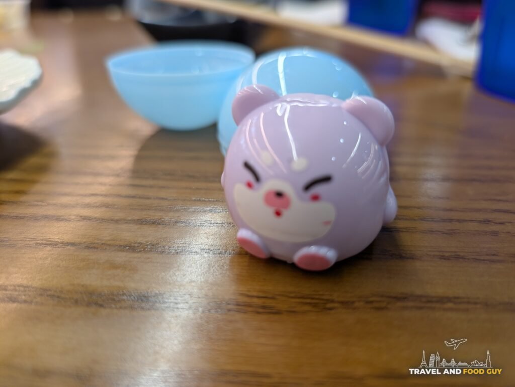 A small purple capsule toy shaped like a round animal sitting on our table next to its open blue capsule.